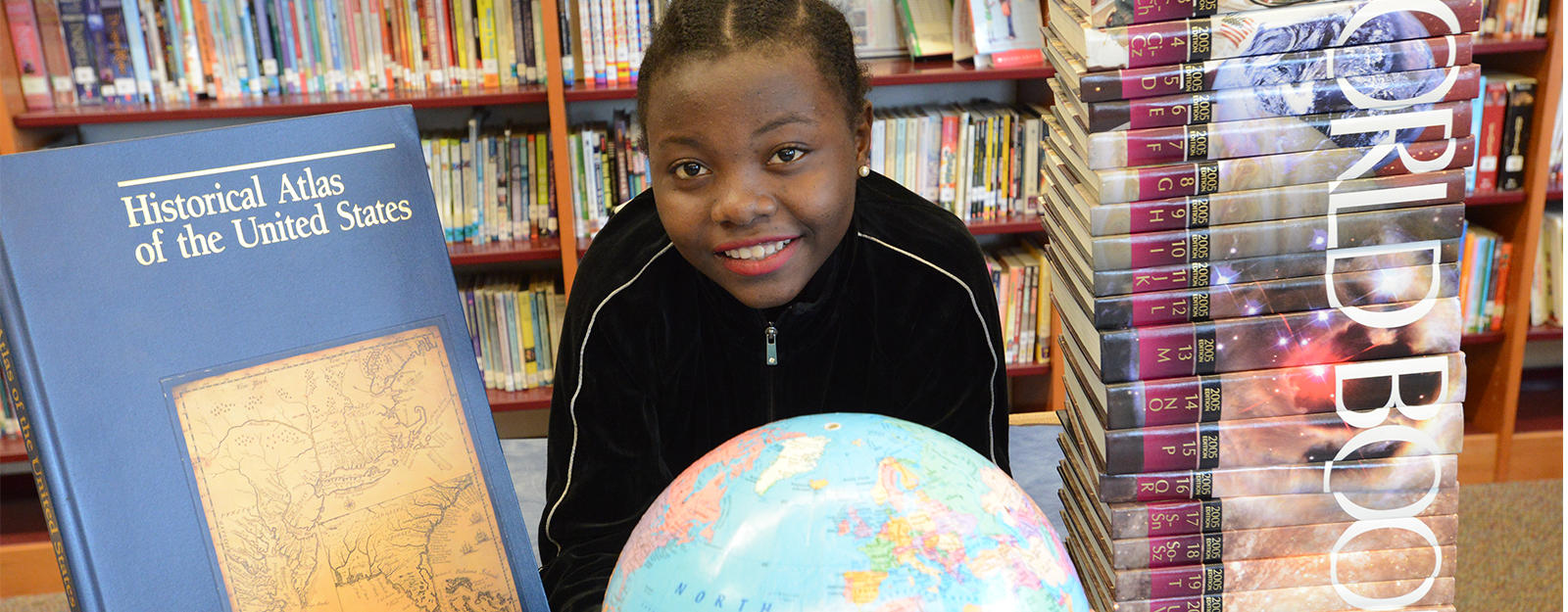 Student smiling behind a globe and stack of history textbooks.